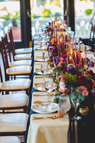 This wedding dining table holds a center row of bouquets colored with red, purple and pink flowers.