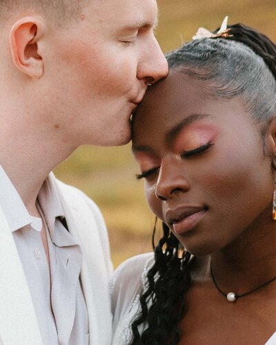 Close-up portrait of a groom kissing his bride on her forehead.