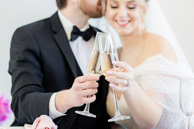 bride and groom cheers with wine glasses in focus in the foreground and the couple out of focus in the background
