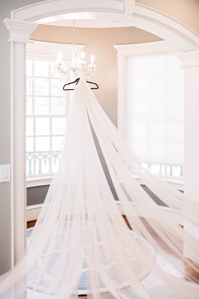 Very long bridal veil hangs from a chandelier in a window alcove.