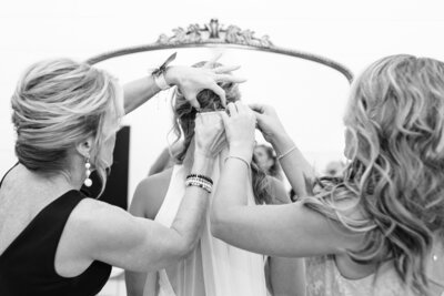 Bride and sister of the bride pinning veil on in front of a large mirror