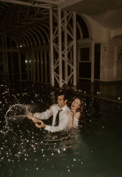 jump in the pool wedding photo of the couple popping champagne in the water