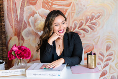 Life Coach on her desk, one hand under a professional book and the other in the chin, smiling