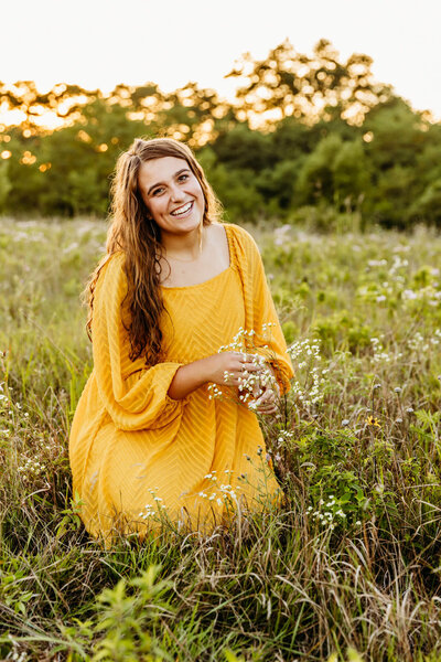 high school senior girl in a yellow dress playing with the wildflowers in a field near Appleton