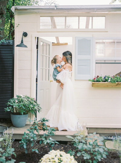 A mother holds her young daughter while standing in a doorway and gives her a kiss during her Washington DC family session