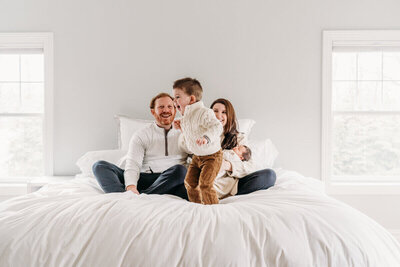 Family enjoying time together on a large white bed, laughing with their children