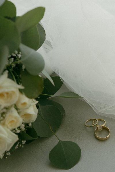 Wedding still life with bridal bouquet, veil, and two gold rings.