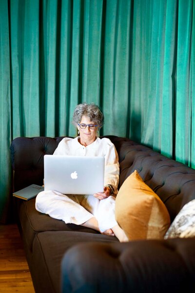 Amy Posner using a laptop while sitting on a sofa against a green curtain background