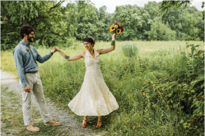 Bride and Groom in a white dress and blue shirt with khaki pants holding hands outside.