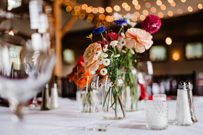 Flowers in vase with table number at center of table, Blended wedding at Peirce Farm at Witch Hill