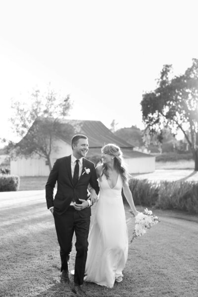 Black and white picture of a couple on their wedding day. she is in a white dress and he is in a suit. they are smiling and laughing together.