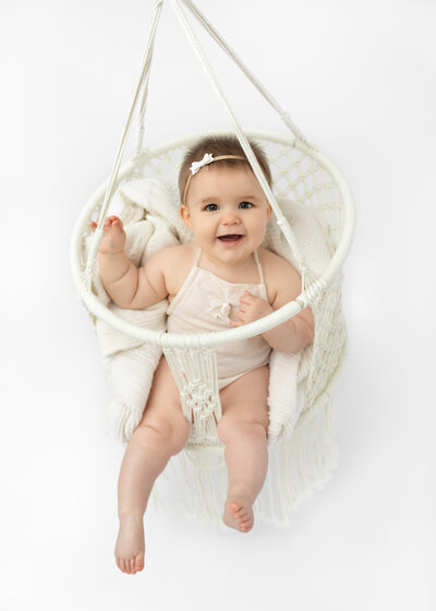 Baby in a macramé swing smiling at the camera during a sitter photoshoot by Hobart Photographer Lauren Vanier