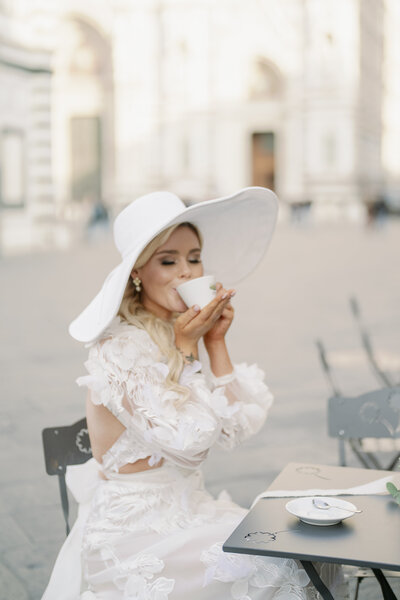 a bride with a giant white hat sipping on an espresso in front of the Duomo in Florence Italy