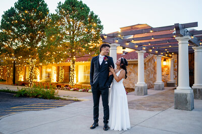 Bride and groom smiling at each other during an evening couples portrait outside a Colorado wedding venue with glowing string lights.