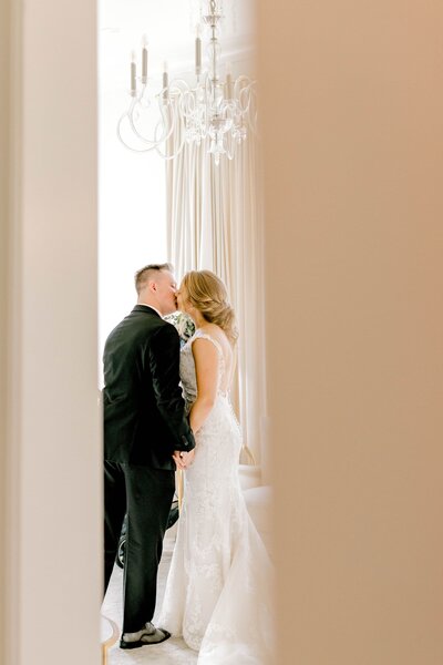 bride and groom kiss behind cracked door