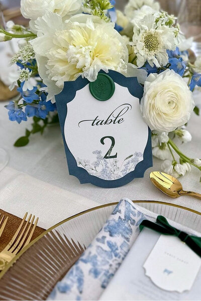 Wedding table number made of soft velvet with a custom wax seal, beautifully placed among lush blue and white floral arrangements for a charming summer wedding in Jackson, WY.