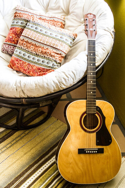 Location Branding Gatos Trail Recording Studio acoustic guitar leaning against round cushion chair on striped rug