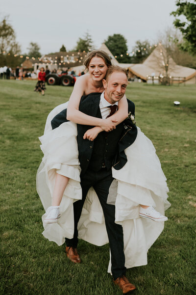 Groom giving bride a piggyback ride at outdoor reception