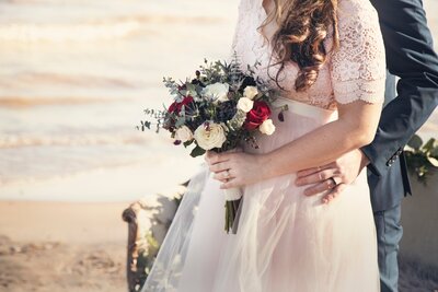 Bride standing by the sea holding bouquet of red and white flowers