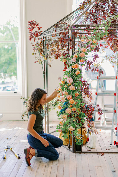 Sara of Wild Child Flower Co. works on wedding arbor installation indoors.