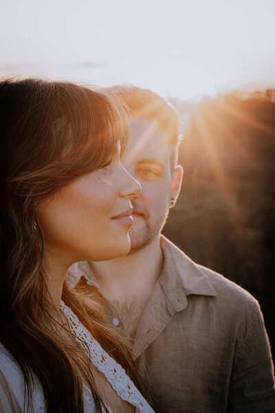 Close up of couple, him facing the camera & her side on to the camera blocking half his face with golden sun flare behind