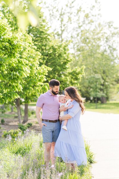 An adorable family posing by some beautiful green trees during spring