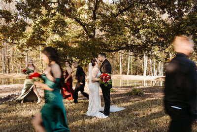 couple kissing underneath trees while wedding party walks by