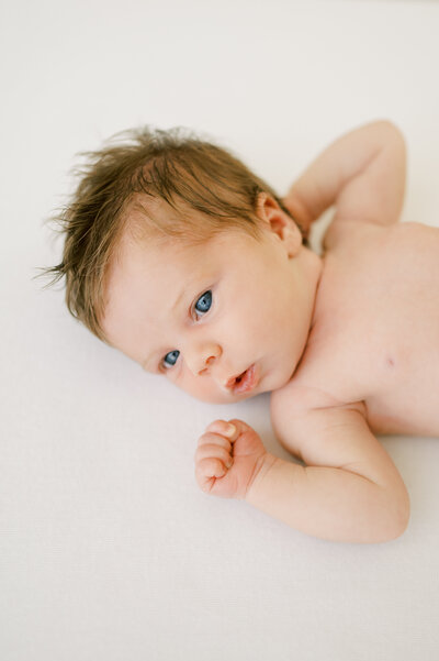 Baby girl with blue eyes lays on white blanket while having photos taken at the Worth Capturing studio in Raleigh NC