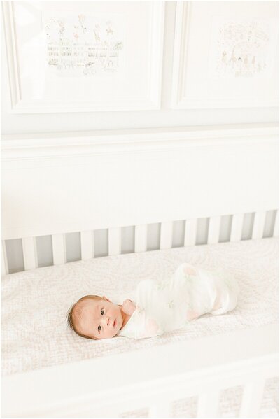 Baby girl swaddled in crib looking at the camera for her newborn photographer session
