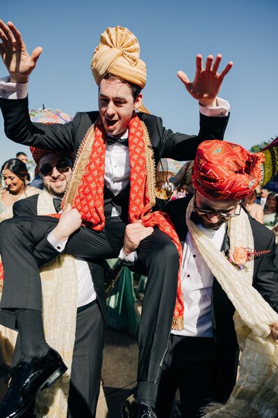 A man in a traditional turban and outfit being lifted in celebration at an event.