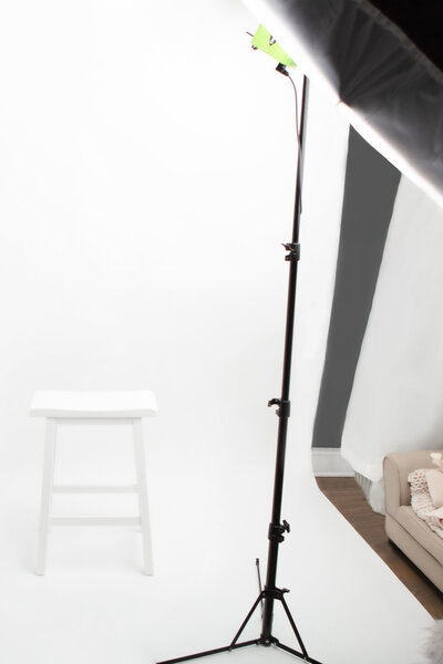 A peek inside the Looking Up Photography studio, located in Greenwich, Connecticut. A large, nearly floor-to-ceiling window bathes the studio in beautiful natural light. The center wall allows for several backdrop options, while a white chaise, rolling stool, and other photography props pepper the studio space.