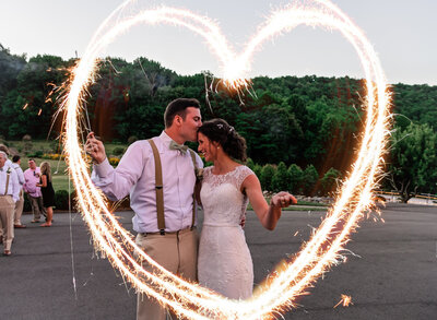 groom kissing brides forehead while making. a heart with sparklers