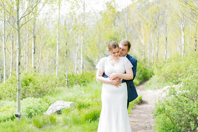 Groom hugging bride from behind, surrounded by aspen trees