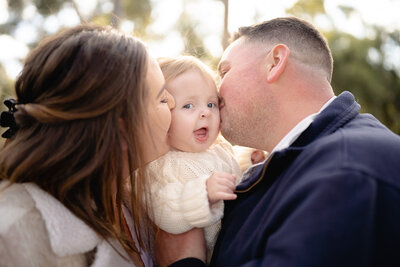 Tender family moment in Geelong with parents kissing their baby girl’s cheeks during a cosy outdoor photography session.