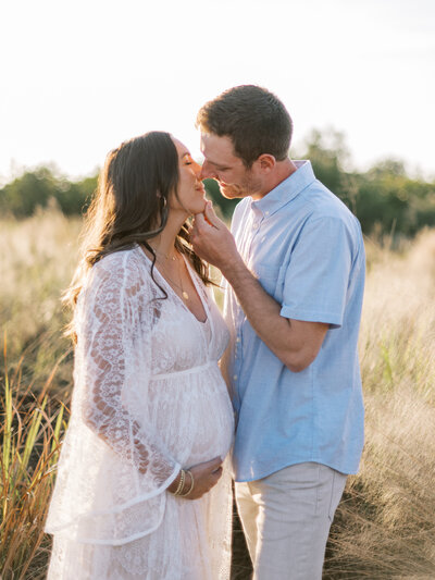 husband kissing pregnant wife in a field