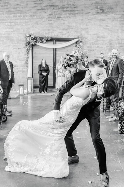 black and white photo of groom dipping and kissing his bride right after wedding ceremony