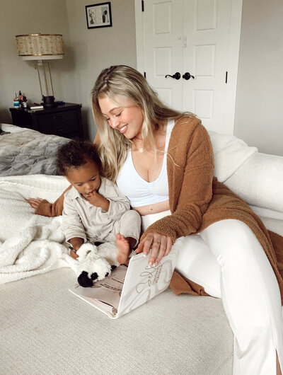Iskra is flipping through the pages of a Self Funding Planner with her toddler on a bed.