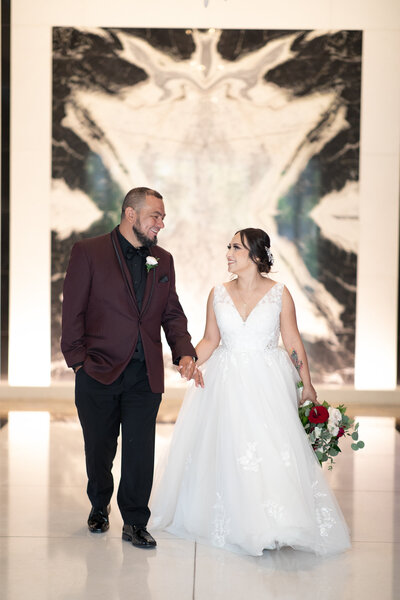 An Austin-based wedding photographer captures a beautiful moment between a bride and groom as they hold hands in front of a large marble wall.