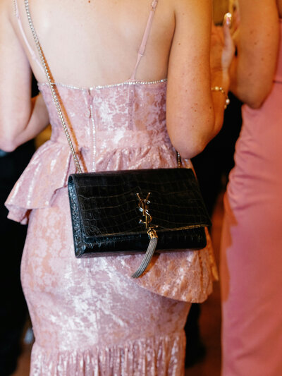 A close-up of a woman in a pink dress holding a black designer clutch, capturing the stylish, upscale atmosphere of a luxury event by Socially Significant Events.