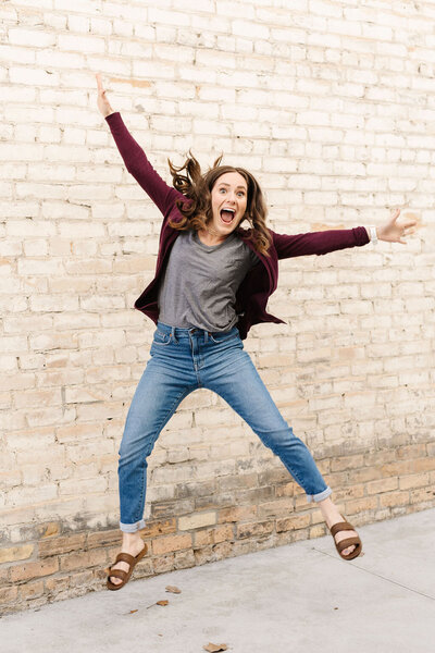 woman doing a starfish jump in front of a brick wall