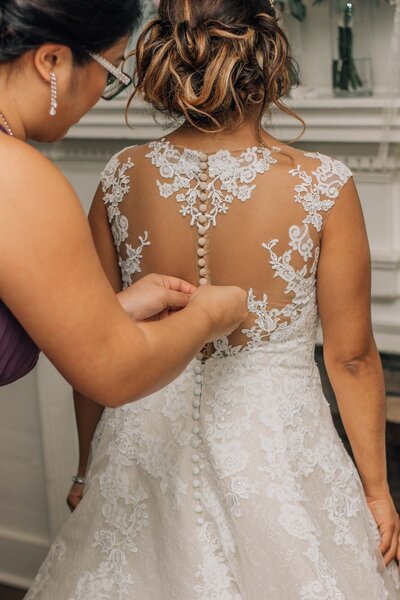 Hampton Roads best wedding photographer captures bride gettign the back of her dress buttoned up by her mother as she gets ready for her Hampton Roads wedding day