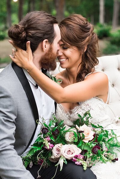 Groom with manbun nuzzling bride with loose braid holdingwhimiscal pink purple and greenery heavy bouquet
