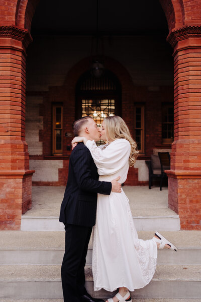Couple embrace and kiss in front of beautiful brick building at Flagler College in St. Augustine, FL. Photo taken by Orlando Wedding Photographer Four Loves Photo and Film.