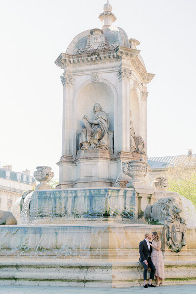 a couple facing each other and standing in front of a large fountain in paris