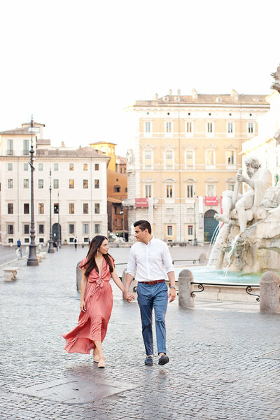 A couple in pastel clothes walking in Piazza Navona. Taken by Rome Anniversary Photographer, Tricia Anne Photography