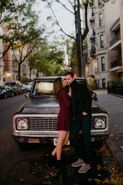couple lease across a classic truck car during their cool and creative low key evening session on a fall day in hoboken new jersey