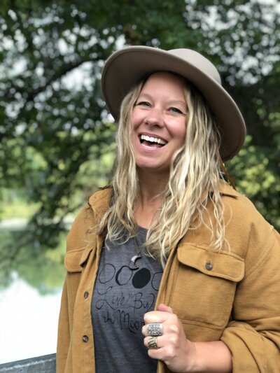 Andrea smiling wearing a brown jacket & hat