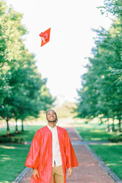 High school senior guy wearing a red gown and throwing his cap high in the air