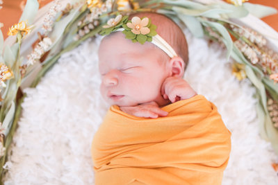 Newborn baby swaddled in yellow swaddle with floral headband sleeps during newborn photography session