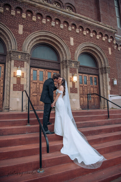 a married couple kissing on the steps of a cathedral